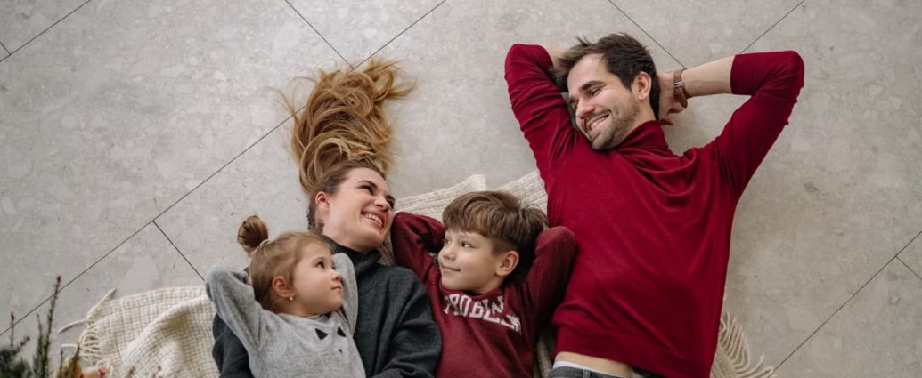 Smiling family of four lying on a blanket, sharing happiness and love indoors.