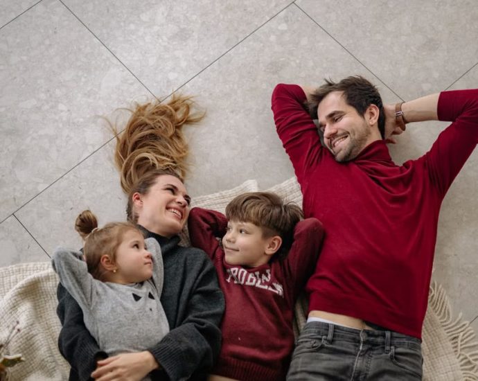 Smiling family of four lying on a blanket, sharing happiness and love indoors.